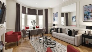 A modern living room with a sofa, red armchairs, a dining table, and a coffee table. - Kensington Apartment | Hyde Park, Portobello, Royal Albert Hall (London)