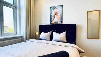 A neatly made bed with white linens, a dark headboard, and a large window with curtains.