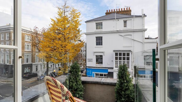 Ein Balkon mit Korbstuhl, einer Topfpflanze und Blick auf ein weißes Gebäude gegenüber.