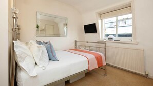 Een slaapkamer met een bed, nachtkastje, spiegel, raam en televisie.