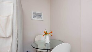 Een kleine, moderne kamer met een glazen tafel, witte stoelen, een witte vaas met bloemen en een ingelijste kaart aan de muur.