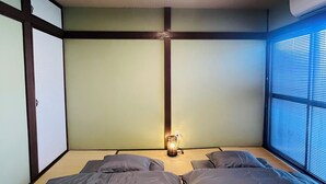 A room with a bed, a wall-mounted air conditioner, and a window with blinds. - THE KAGAYA KYOTO hachijokuchi (Kyoto)