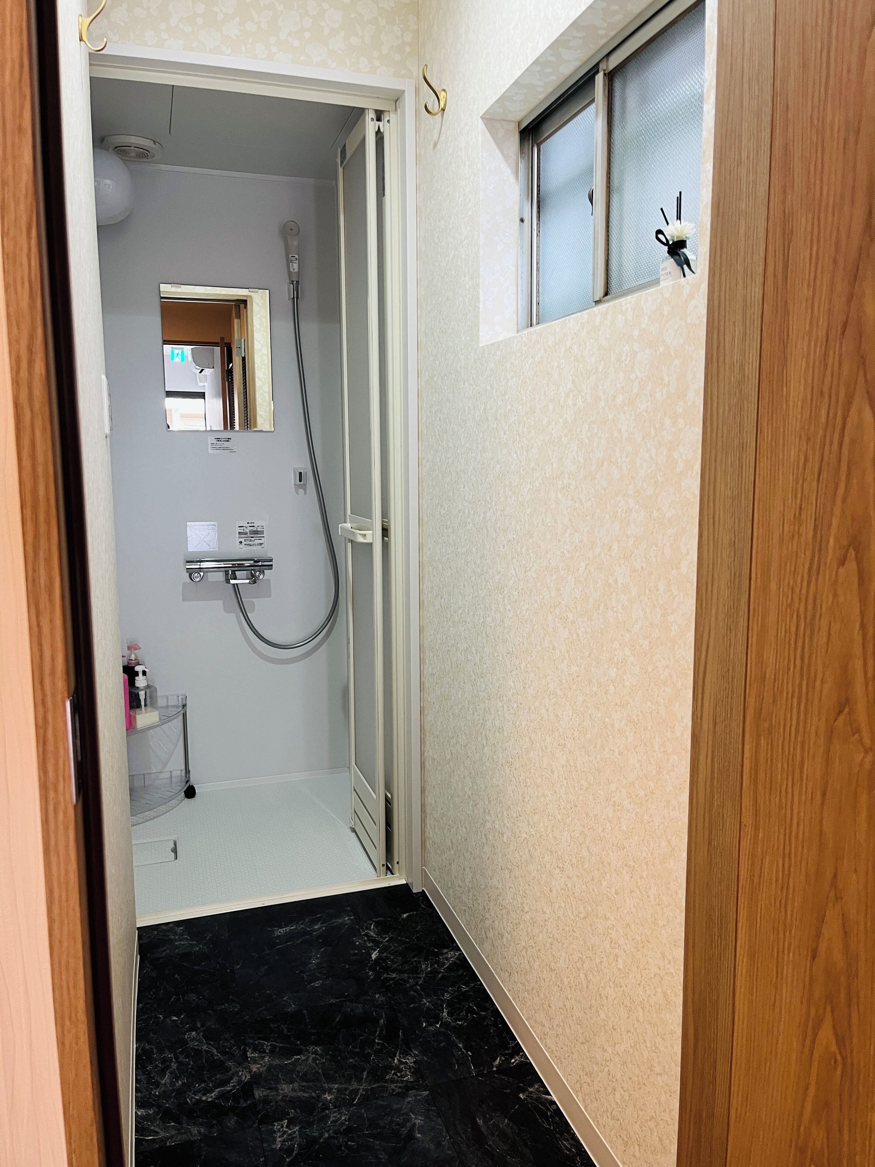 A narrow hallway leading to a bathroom with a shower, a small shelf with toiletries, and a window with a decorative item.