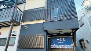 A building with a dark facade, a balcony with metal railings, and a blue entrance with Japanese characters. - THE KAGAYA KYOTO hachijokuchi (Kyoto)