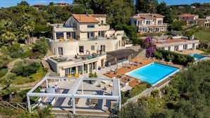 Una villa moderna con una gran piscina, varios balcones y abundante vegetación a su alrededor.