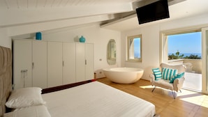 Un dormitorio moderno con una cama grande, un armario empotrado, una bañera independiente, un televisor y un balcón con vistas.
