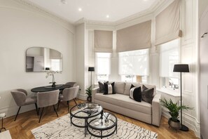 A modern living room with a sofa, coffee table, and dining area. - Elegant South Kensington Apartment by Hyde Park and Harrods (South Kensington)
