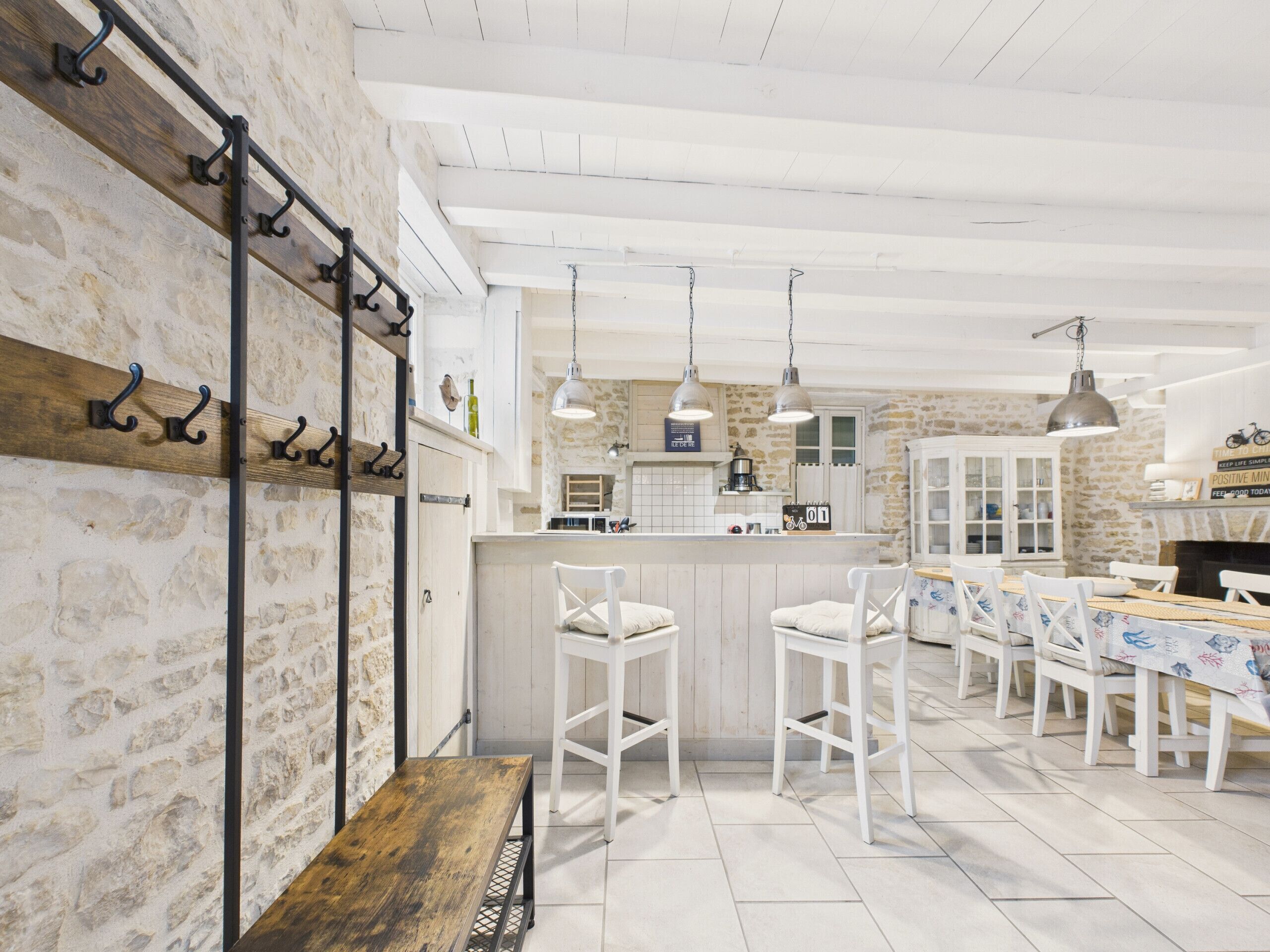 A spacious kitchen with white cabinetry, a wooden bench, and a dining area with white chairs.