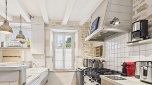 A kitchen with a gas stove, oven, and various appliances. There is a window with a view of greenery outside. - Charming house for 8 people, 800m from the beach (Le Bois-Plage-en-Ré)