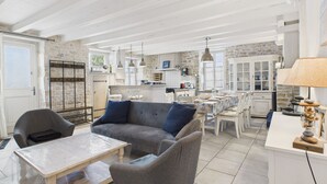 A spacious living area with a sofa, chairs, a coffee table, and a kitchen in the background. - Charming house for 8 people, 800m from the beach (Le Bois-Plage-en-Ré)