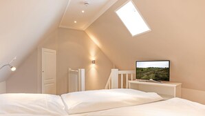 A bedroom with a sloped ceiling, a skylight, a bed, a bedside table with a television, and a white door. - Modern premium vacation apartment under thatch with garden, sauna and pool (Keitum)