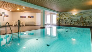 An indoor swimming pool with clear water, wooden ceiling, and a mural on the wall. - Modern premium vacation apartment under thatch with garden, sauna and pool (Keitum)