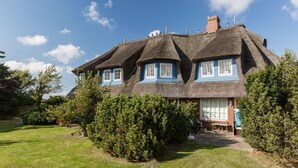 A traditional thatched-roof house with multiple windows and a well-maintained garden. - Modern premium vacation apartment under thatch with garden, sauna and pool (Keitum)