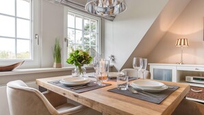 A dining area with a wooden table set for two, a vase with flowers, and a modern lamp. - Modern premium vacation apartment under thatch with garden, sauna and pool (Keitum)