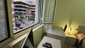 Ein Zimmer mit Blick auf eine Straße, ein kleiner Tisch mit Fernbedienung und eine Nachttischlampe.
