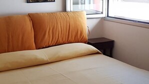 A bed with a beige and orange headboard in a room with a window and a small table. - Villa 'Tra Cielo E Sabbia 2' with Sea View, Private Terrace and Air Conditioning (San Vito Lo Capo)