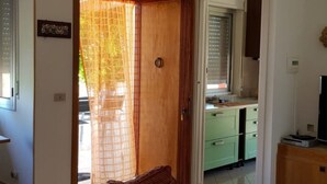 A room with a wooden door, a window with blinds, a green cabinet, and a television on a wooden stand. - Villa 'Tra Cielo E Sabbia 2' with Sea View, Private Terrace and Air Conditioning (San Vito Lo Capo)