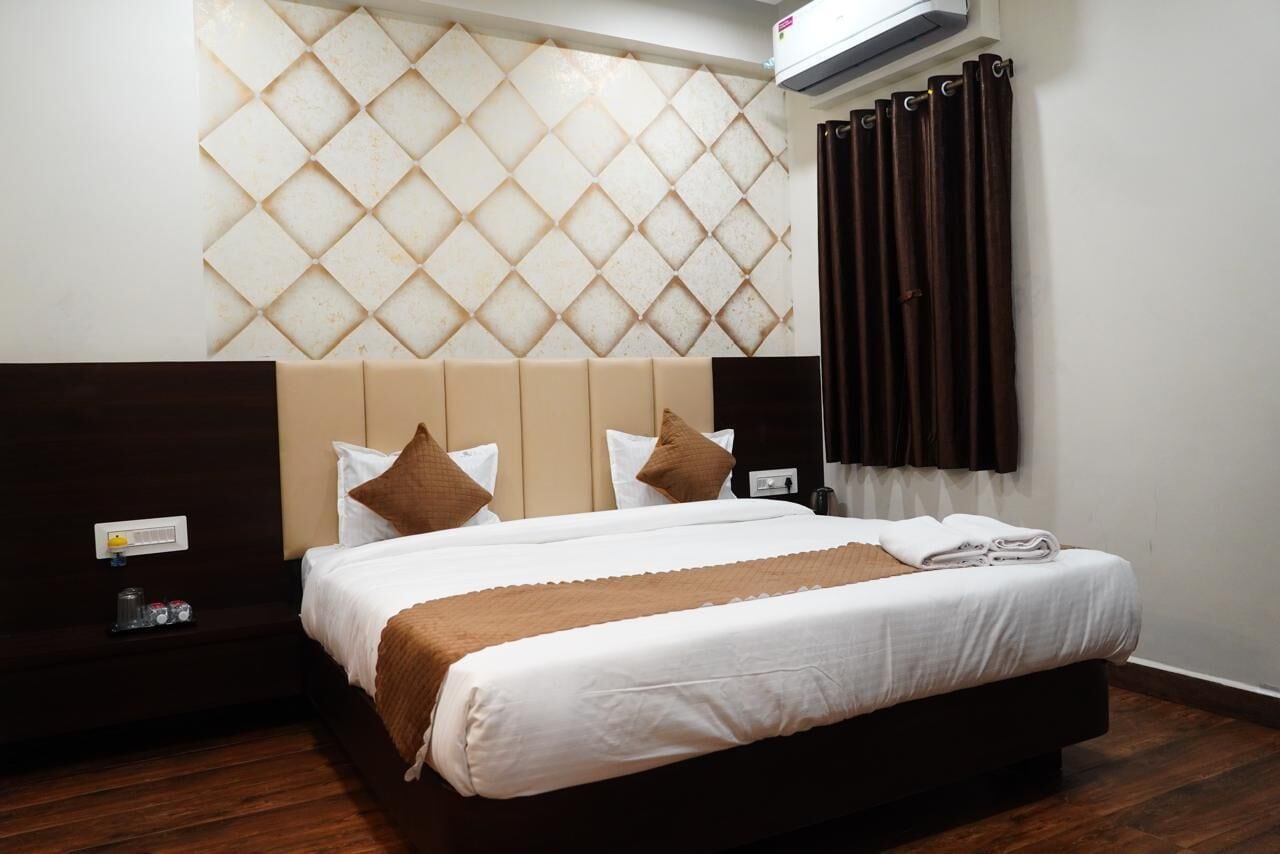 Een hotelkamer met een groot bed, een hoofdbord met een diamantpatroon, een nachtkastje met een lamp en een raam met gordijnen.