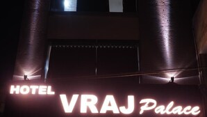 La entrada al Hotel VRAJ Palace, con un mostrador de recepción, un área de descanso y una escalera que conduce al interior.