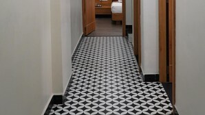 Un pasillo de hotel con piso a cuadros, puertas de madera y una cama al fondo.