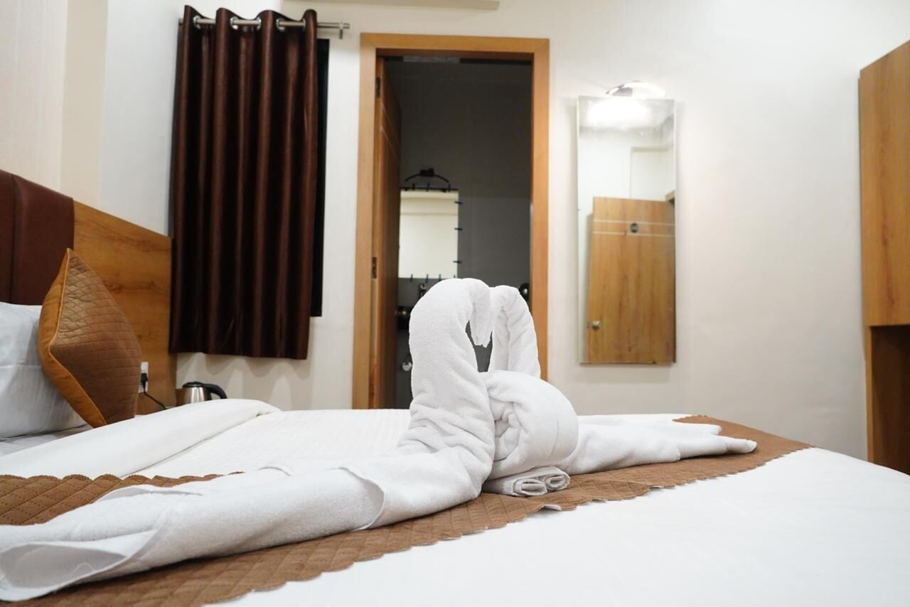 Cama bem arrumada com colcha marrom, cabeceira de madeira e cortina marrom.
