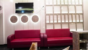 Zona de recepción con un sofá rojo, un televisor en la pared y un panel decorativo con elementos circulares y rectangulares.