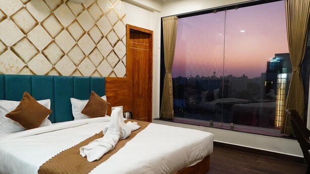 Habitación de hotel con una cama grande, vistas a la ciudad al atardecer y un diseño moderno.