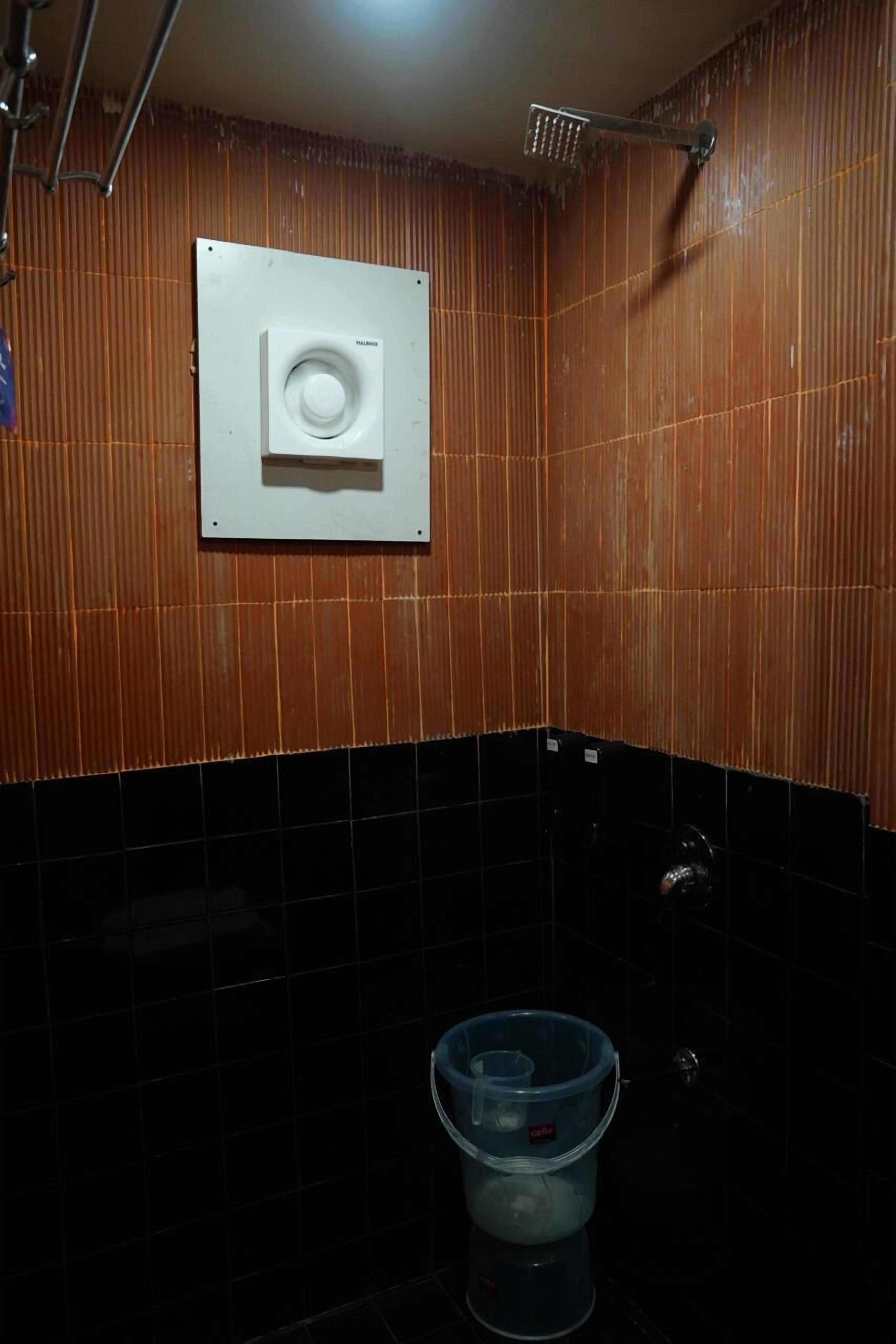 A bathroom with a wooden wall, a white vent, and a black tiled floor.