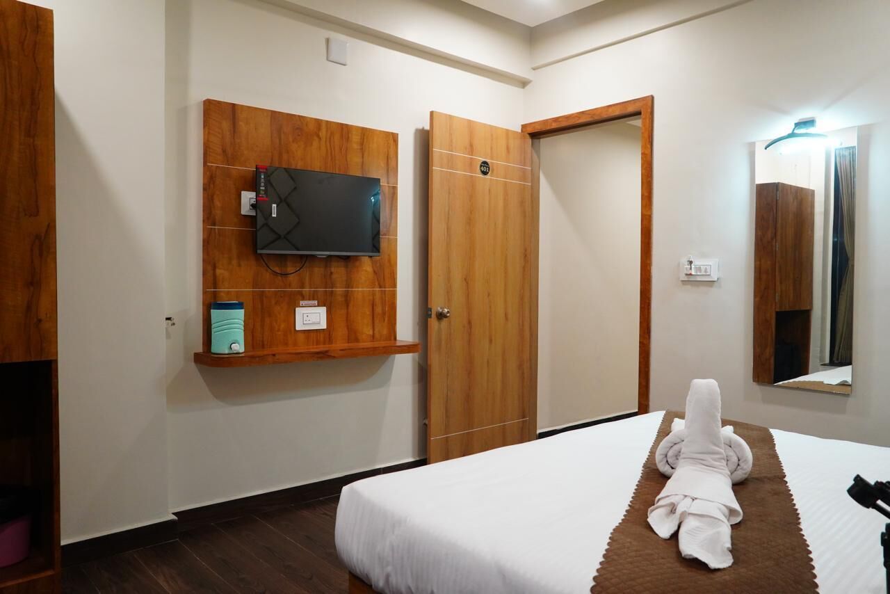A hotel room with a bed, a television mounted on the wall, a wooden wardrobe, and a mirror.