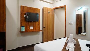 A hotel room with a bed, a television mounted on the wall, a wooden wardrobe, and a mirror.