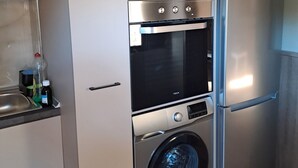 Eine kompakte Küche mit Einbauofen, Waschmaschine und Kühlschrank.