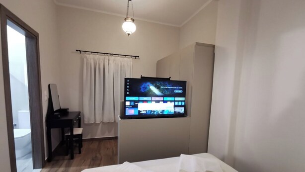 Ein Hotelzimmer mit Bett, Schreibtisch, Stuhl, einem an der Wand befestigten Fernseher und einem Fenster mit Vorhängen.