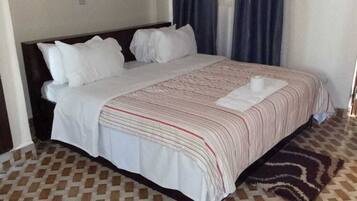 Una cama bien hecha con una colcha a rayas y almohadas, una alfombra estampada y una puerta a la derecha.