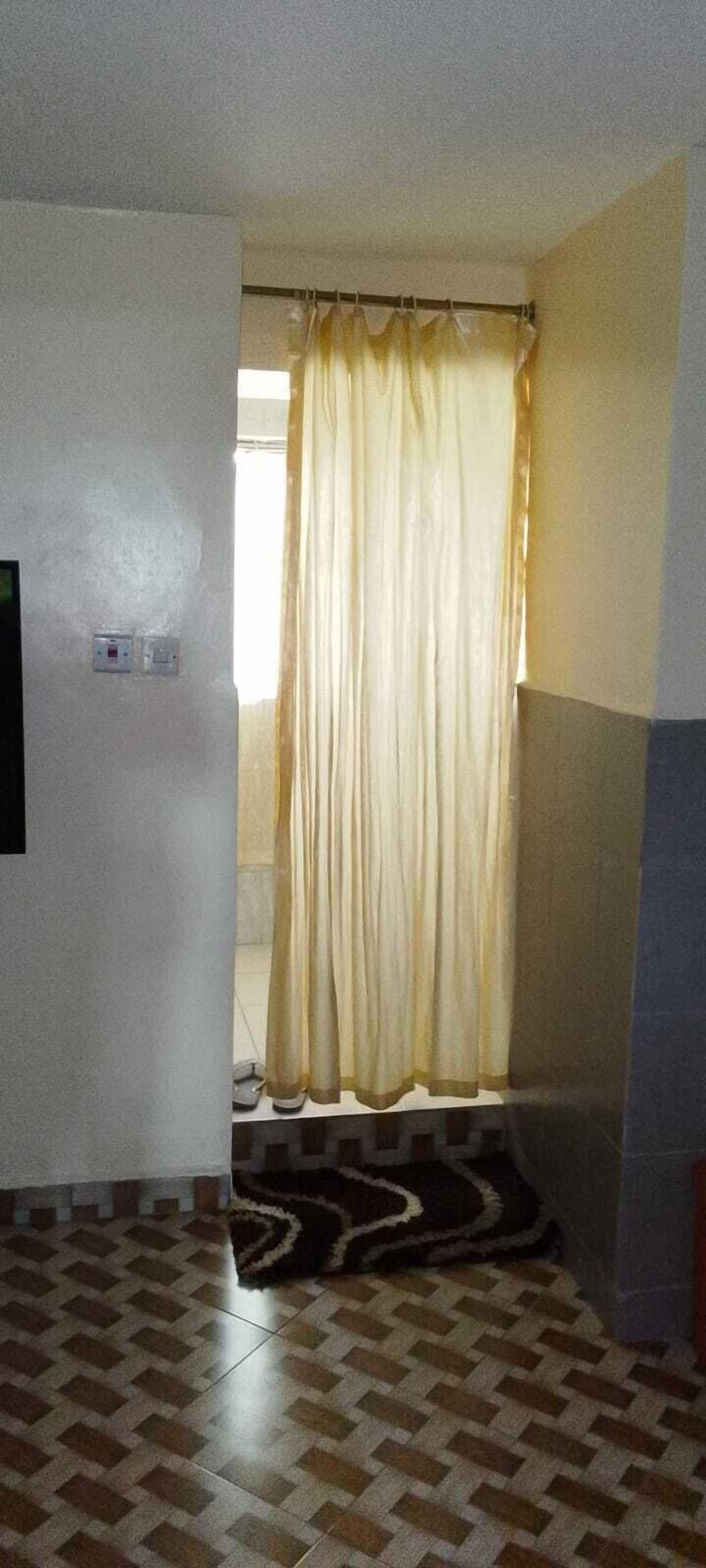 A room with a patterned floor, a curtain, and a wall-mounted light switch.