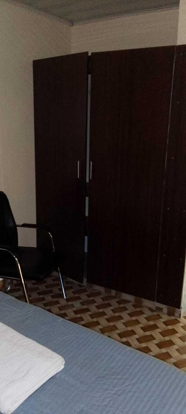 A room with a bed, a chair, and a wardrobe. - Koyaro Centre (Nairobi)