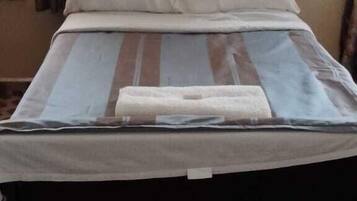 Una cama con una colcha a rayas, dos almohadas y una manta doblada. La habitación tiene un suelo de cuadros y una ventana con cortinas.