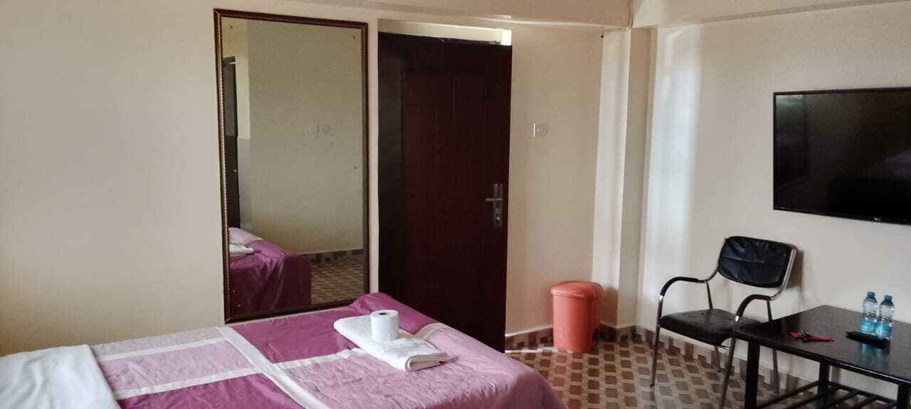 Una habitación de hotel con cama, espejo, televisión, escritorio con silla y cubo de basura.