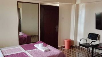 Una habitación de hotel con cama, espejo, televisión, escritorio con silla y cubo de basura.