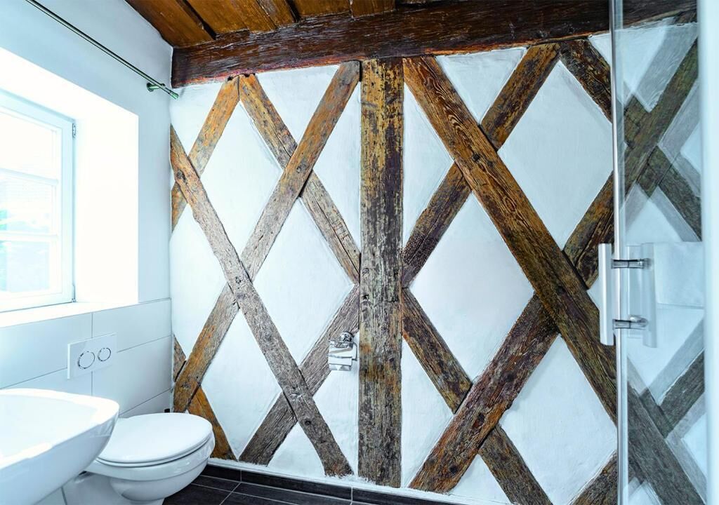 A bathroom with a rustic wooden wall design, a white toilet, and a glass shower enclosure.