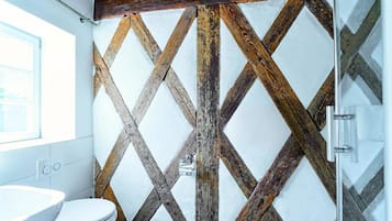 Un bagno con rivestimento murale in legno rustico, un WC bianco e un box doccia in vetro.