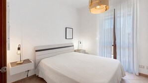 A bedroom with a bed, bedside lamps, a wall-mounted picture, and a window with curtains. - Holiday Home 'A Casa Di Titti' with Mountain View, Wi-Fi, and Air Conditioning (San Vito Lo Capo)