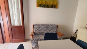 A room with a wooden door, a patterned chair, a table, and a painting of yellow flowers on the wall. - Casa Sole di Sicilia: Sea View, Wi-Fi & Air Conditioning in San Vito Lo Capo (San Vito Lo Capo)