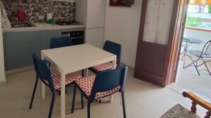 A dining area with a white table and blue chairs, a kitchen with patterned backsplash, and a view of the outside. - Casa Sole di Sicilia: Sea View, Wi-Fi & Air Conditioning in San Vito Lo Capo (San Vito Lo Capo)