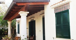 A building with a covered porch supported by columns, a door with a decorative tile border, and a window with shutters. - Villetta Sole: Holiday Home with Mountain View, Shared Terrace & Air Conditioning (San Vito Lo Capo)