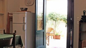 An open door leading to a patio with a table and chairs, a refrigerator, and a clock on the wall. - Villetta Sole: Holiday Home with Mountain View, Shared Terrace & Air Conditioning (San Vito Lo Capo)
