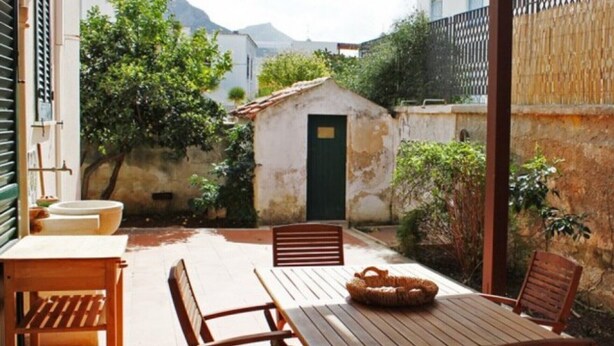 A patio with a table and chairs, a small shed, and a view of a mountain. - Villetta Sole: Holiday Home with Mountain View, Shared Terrace & Air Conditioning (San Vito Lo Capo)
