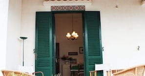 A doorway with green shutters, a chandelier, and wicker furniture. - Villetta Sole: Holiday Home with Mountain View, Shared Terrace & Air Conditioning (San Vito Lo Capo)