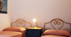 A bedroom with two beds, a nightstand with a lamp, and a wall painting. - Villetta Sole: Holiday Home with Mountain View, Shared Terrace & Air Conditioning (San Vito Lo Capo)