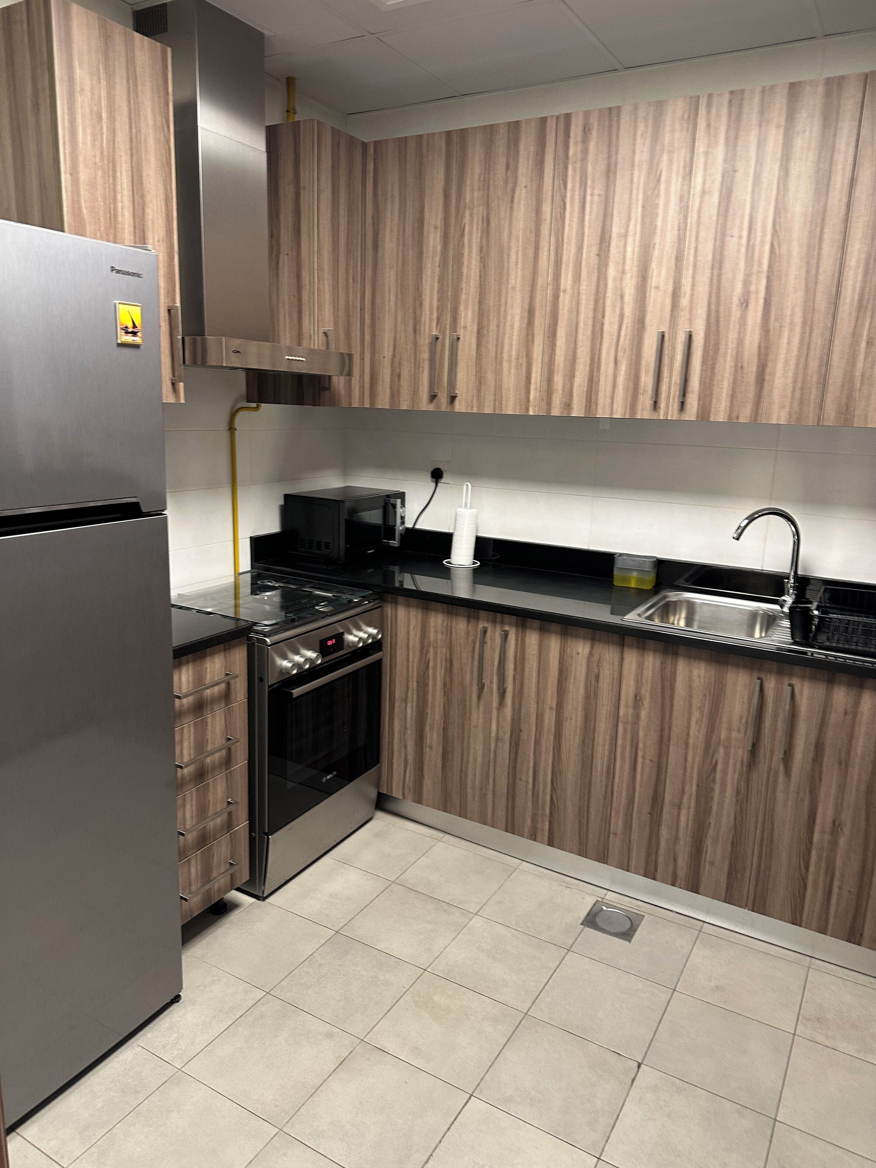 Une cuisine moderne dotée de meubles avec des panneaux en bois, d’appareils électroménagers en acier inoxydable et d’un plan de travail noir.