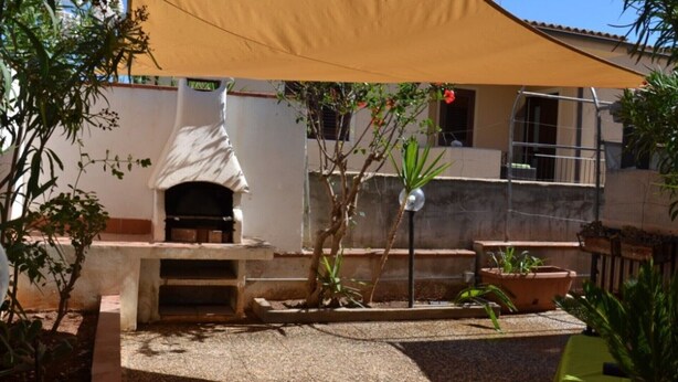 A courtyard with a stone fireplace, potted plants, and a pergola providing shade.